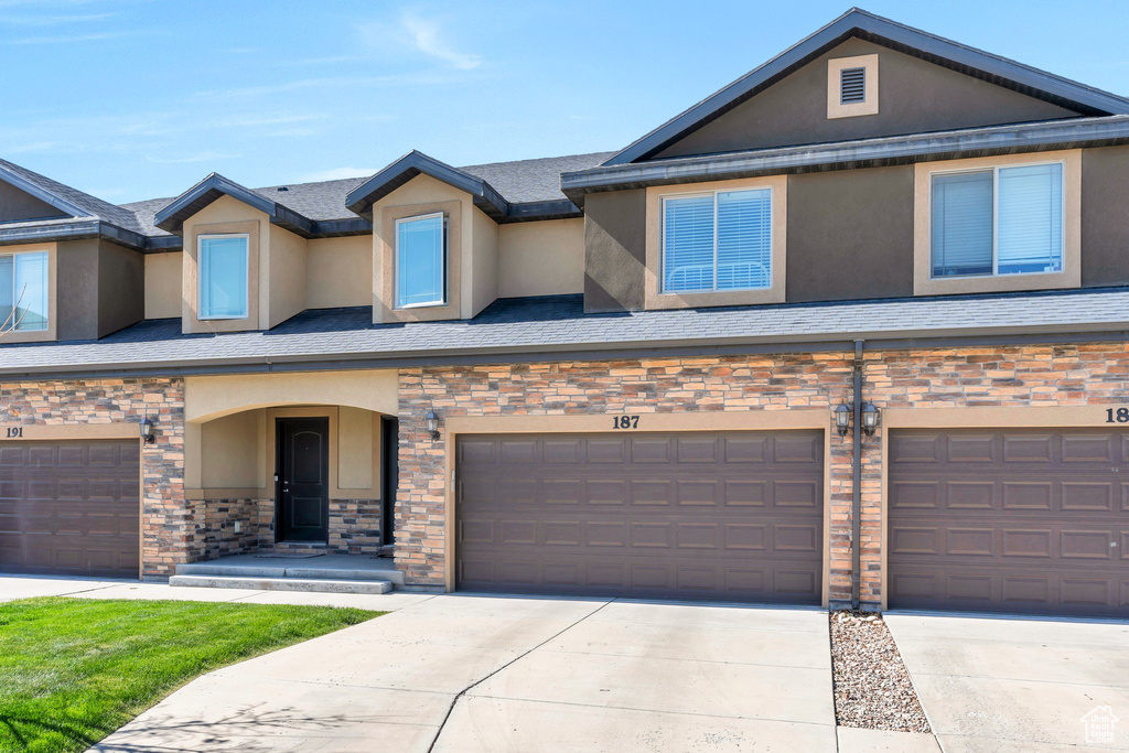 Multi unit property with stone siding, stucco siding, driveway, and an attached garage