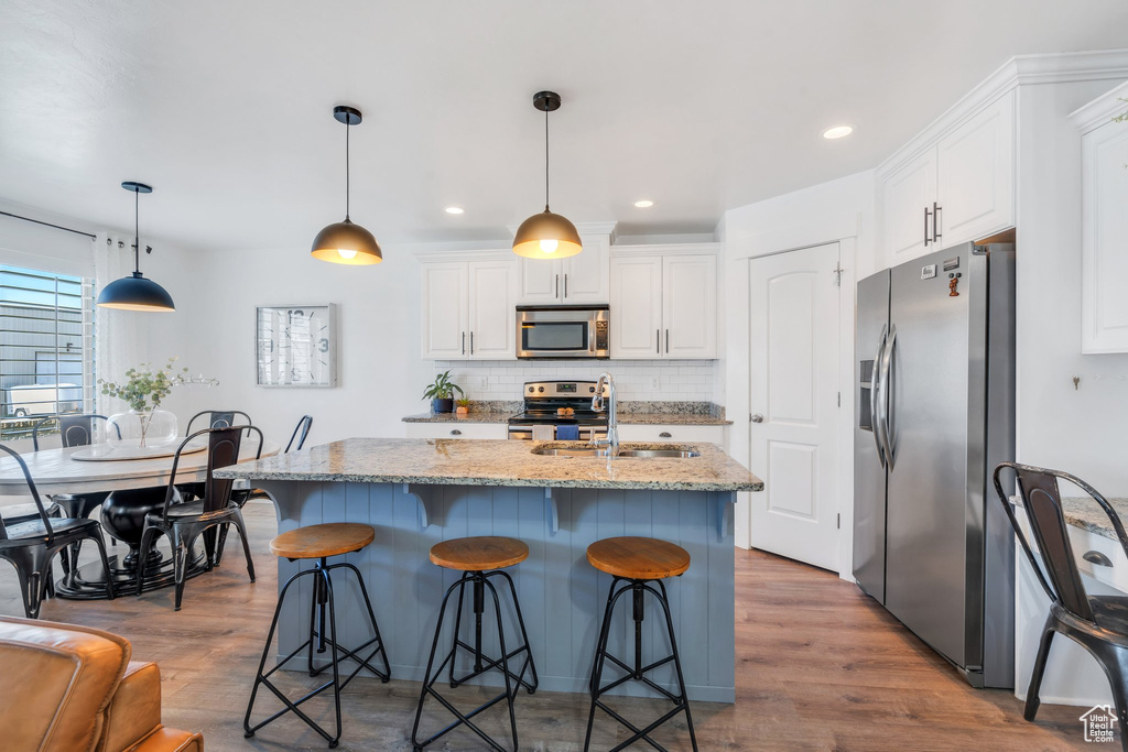 Kitchen with stainless steel appliances, a sink, white cabinets, wood finished floors, and tasteful backsplash