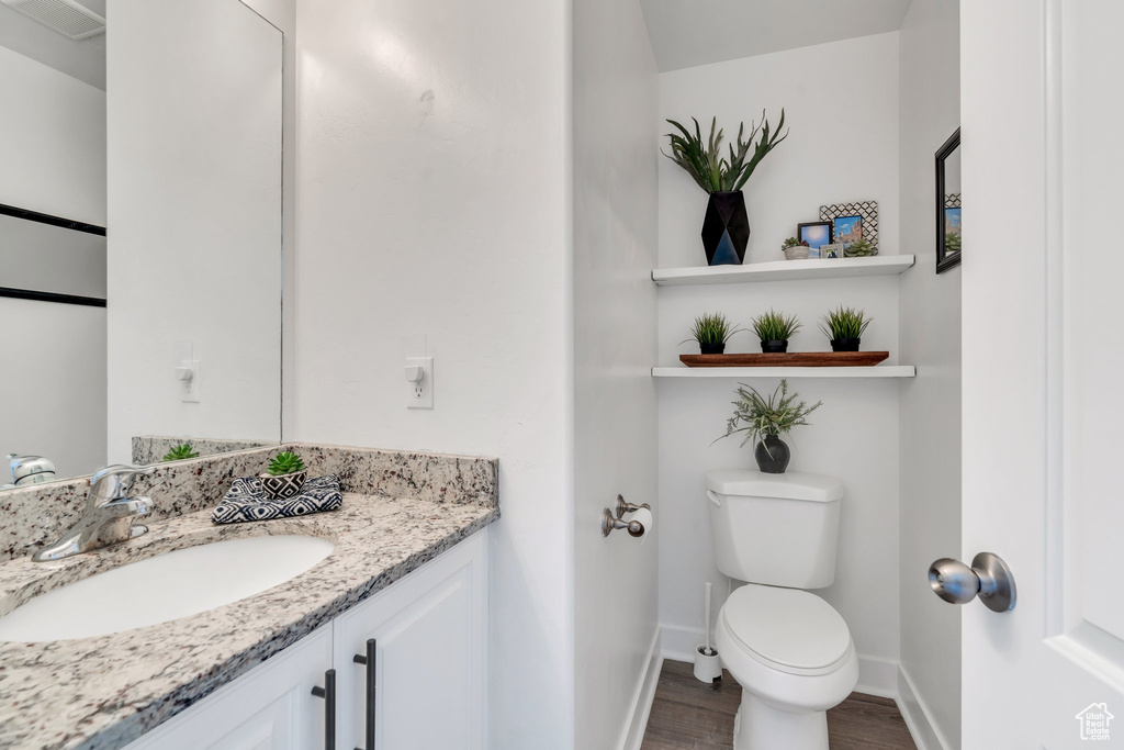 Half bath featuring toilet, wood finished floors, vanity, and baseboards