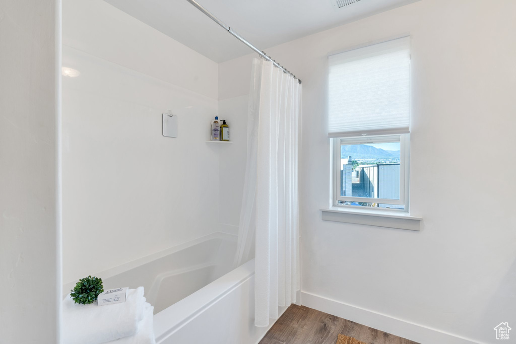 Full bath with wood finished floors, shower / tub combo with curtain, and baseboards
