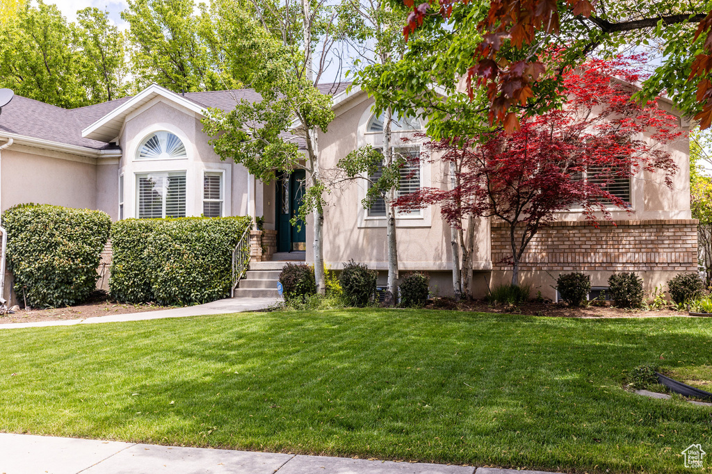 View of front of house featuring stucco siding, a front yard, and roof with shingles