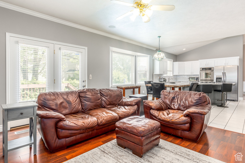 Living area with a ceiling fan, healthy amount of natural light, crown molding, lofted ceiling, and light wood-style floors