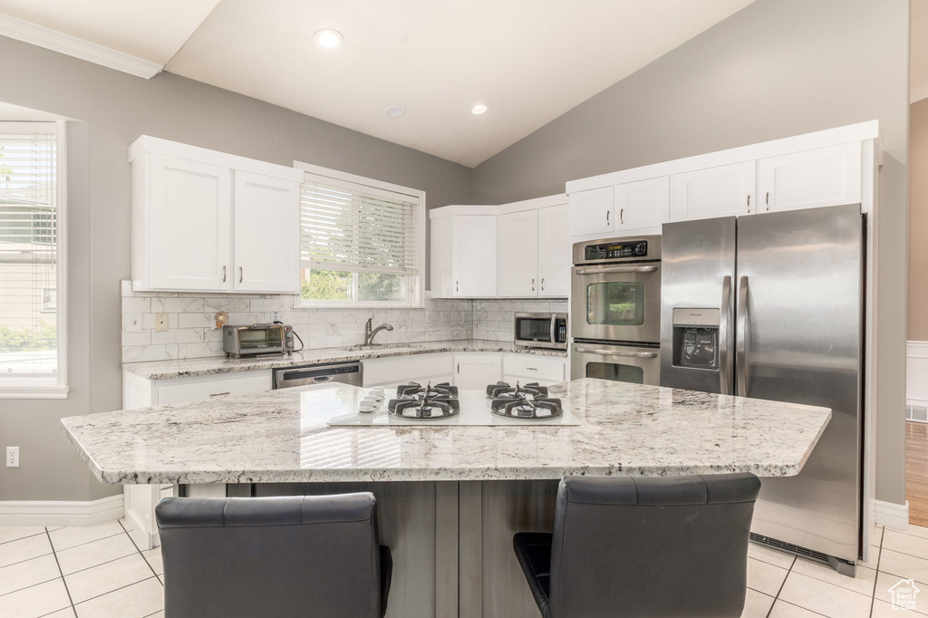 Kitchen with appliances with stainless steel finishes, light tile patterned flooring, a kitchen bar, tasteful backsplash, and vaulted ceiling