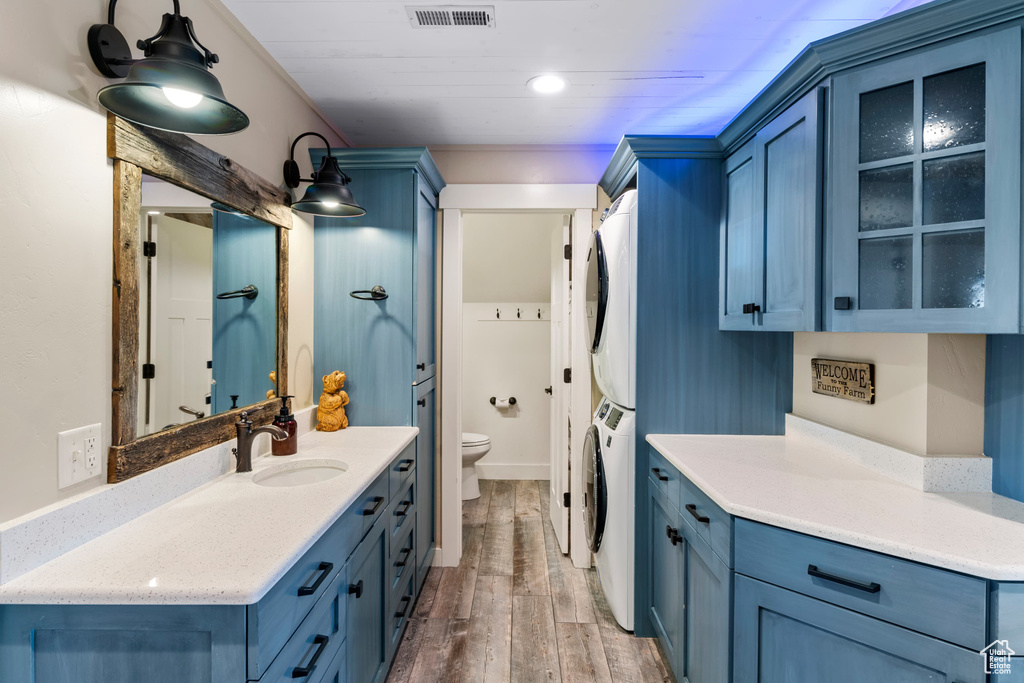 Full bathroom with stacked washer / drying machine, toilet, vanity, and wood finished floors