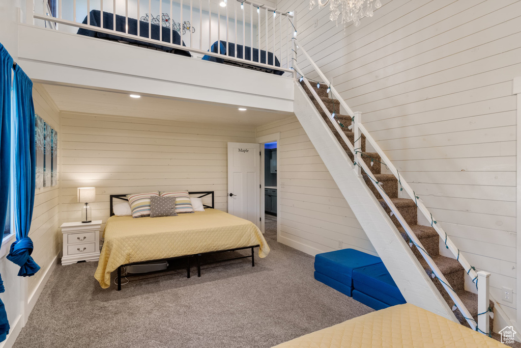 Bedroom with carpet, wood walls, a towering ceiling, and baseboards