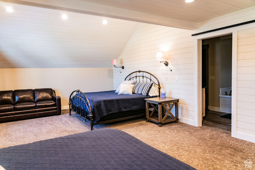 Carpeted bedroom with vaulted ceiling, wood walls, recessed lighting, baseboards, and ensuite bath