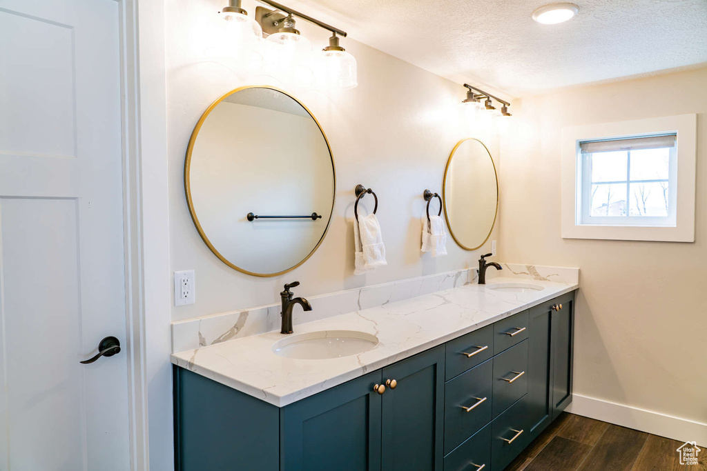 Bathroom with double vanity, a textured ceiling, wood finished floors, and baseboards