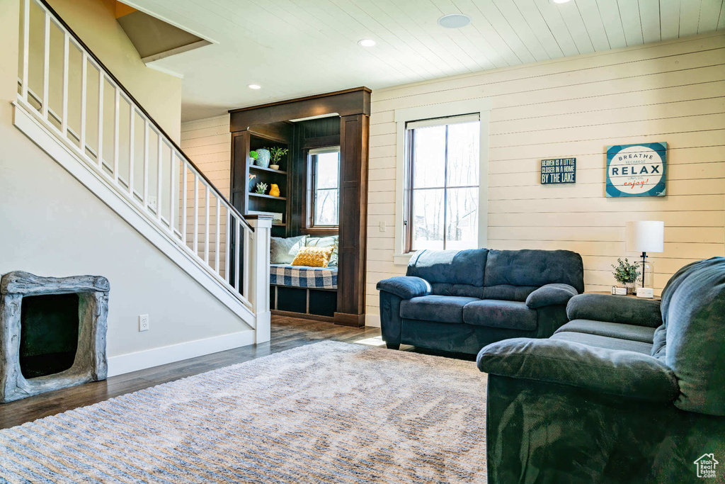 Living room with recessed lighting, wooden walls, wood finished floors, stairway, and baseboards
