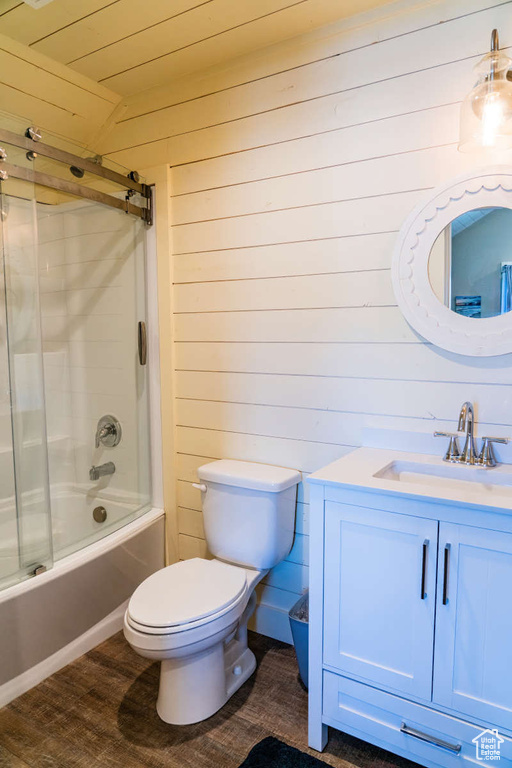 Full bathroom featuring wooden walls, toilet, vanity, shower / bath combination with glass door, and wood finished floors