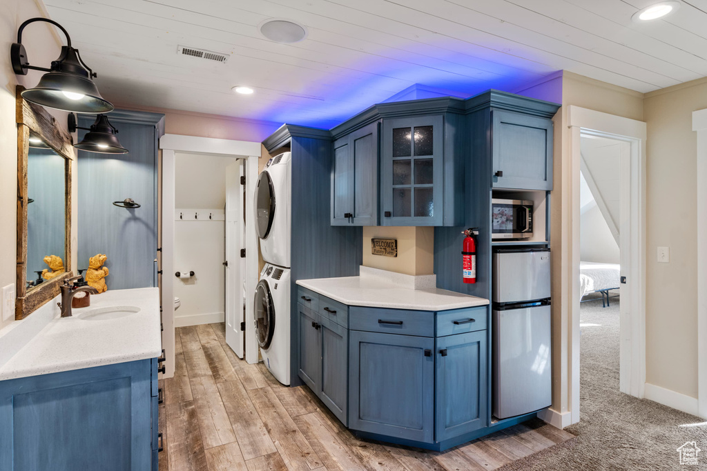 Laundry room featuring stacked washing machine and dryer, recessed lighting, wood ceiling, baseboards, and light wood-type flooring