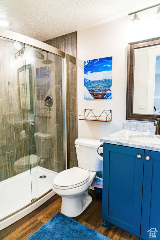 Full bathroom with vanity, toilet, a textured ceiling, a stall shower, and wood finished floors