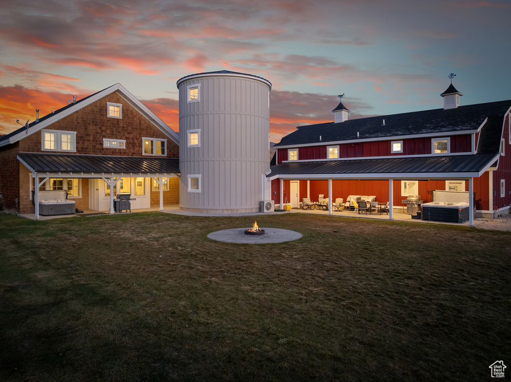 Back of property at dusk featuring a hot tub, a fire pit, a patio area, and a yard