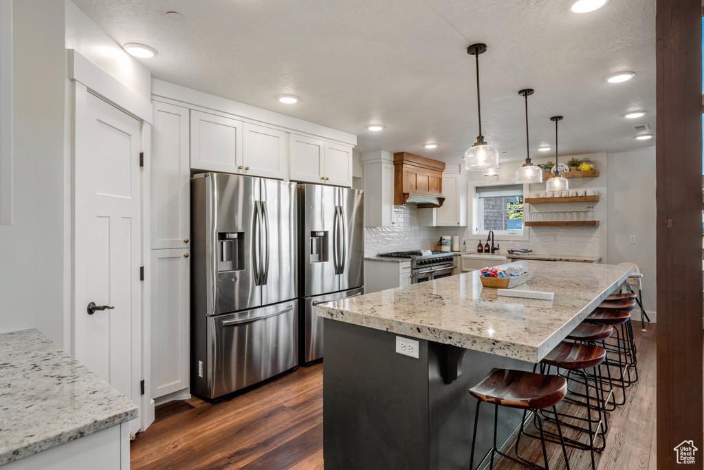 Kitchen featuring stainless steel appliances, dark wood-type flooring, a kitchen bar, white cabinets, and recessed lighting