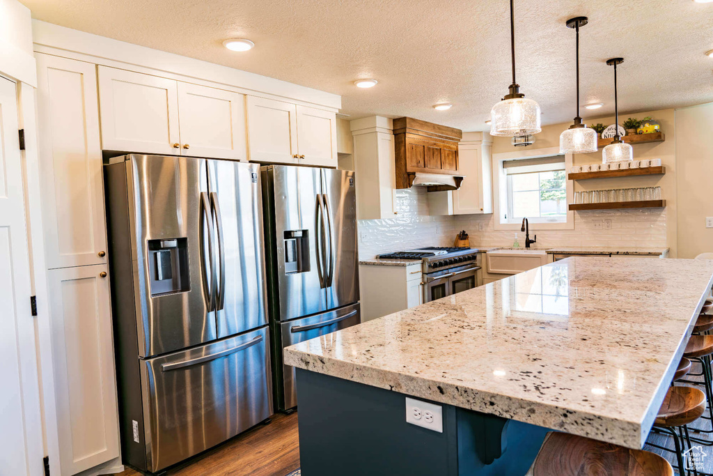 Kitchen with appliances with stainless steel finishes, a kitchen breakfast bar, open shelves, a sink, and a textured ceiling