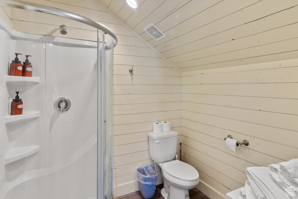 Bathroom with vaulted ceiling, wooden walls, a shower stall, wooden ceiling, and toilet