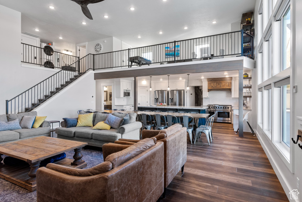 Living area with a towering ceiling, dark wood-style flooring, stairs, recessed lighting, and a ceiling fan