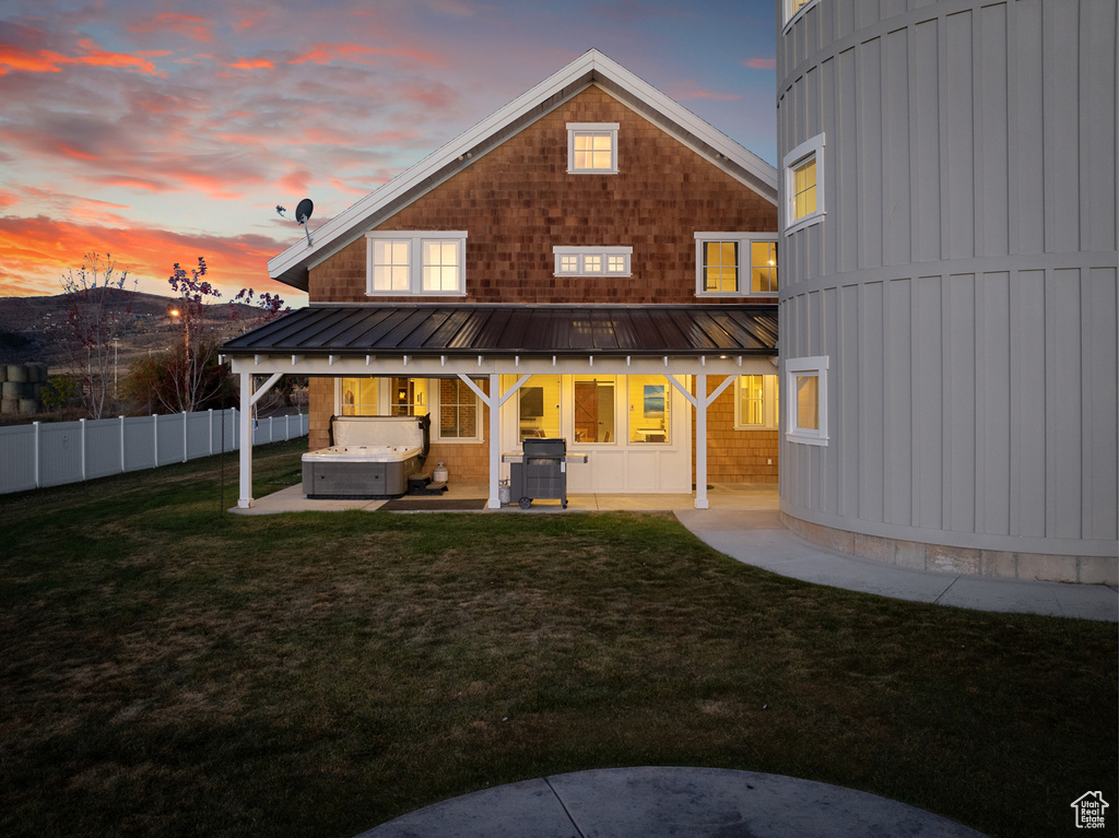 Back of property at dusk with a hot tub, a patio, a standing seam roof, and metal roof