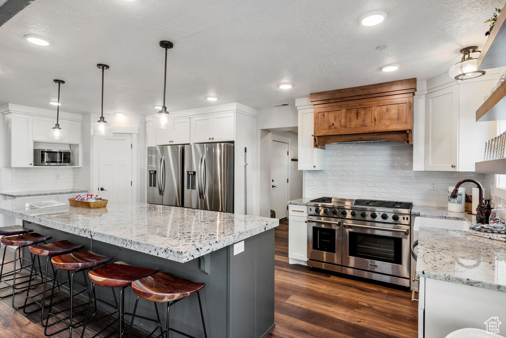 Kitchen with stainless steel appliances, white cabinets, decorative backsplash, light stone counters, and a textured ceiling