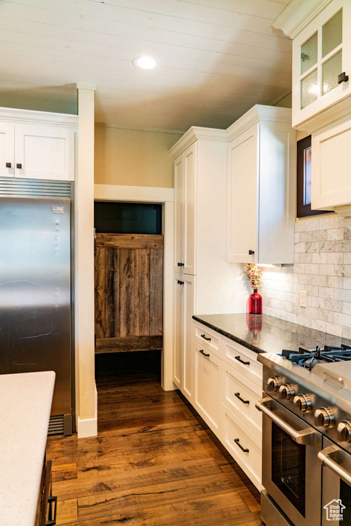 Kitchen with appliances with stainless steel finishes, white cabinetry, decorative backsplash, dark wood-style floors, and glass insert cabinets