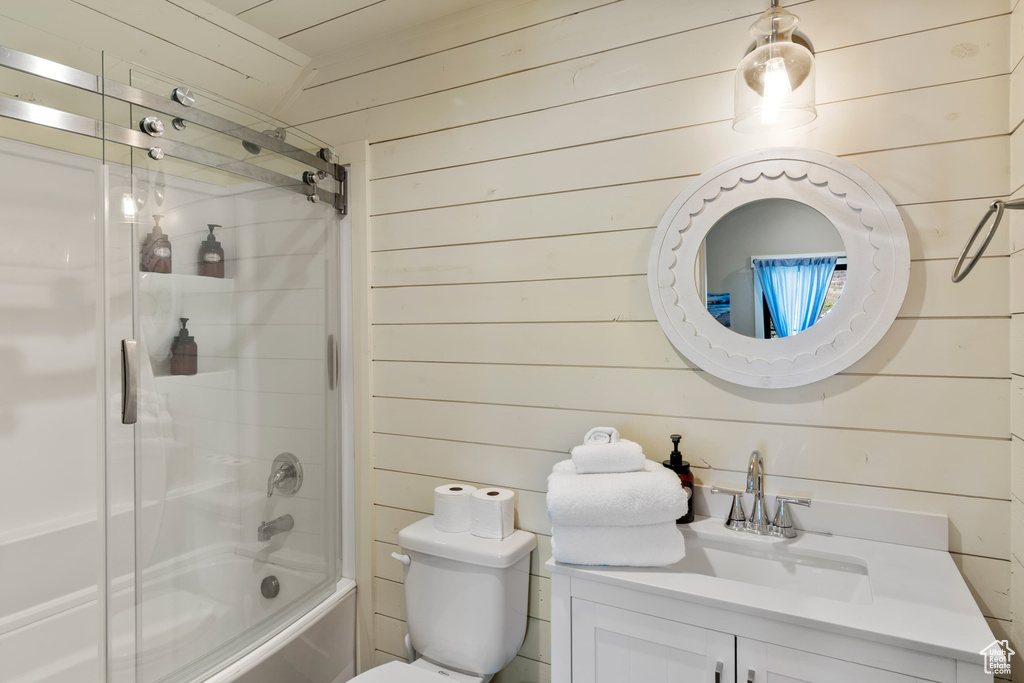 Bathroom with wood walls, vanity, shower / bath combination with glass door, and toilet