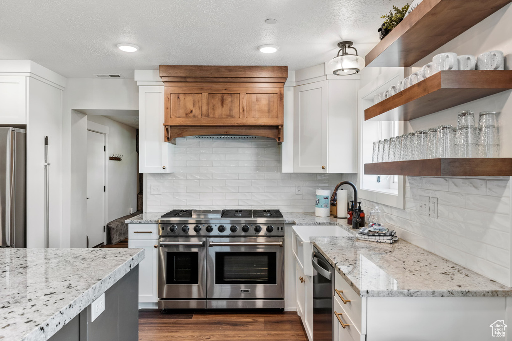Kitchen featuring stainless steel appliances, open shelves, white cabinets, light stone countertops, and tasteful backsplash