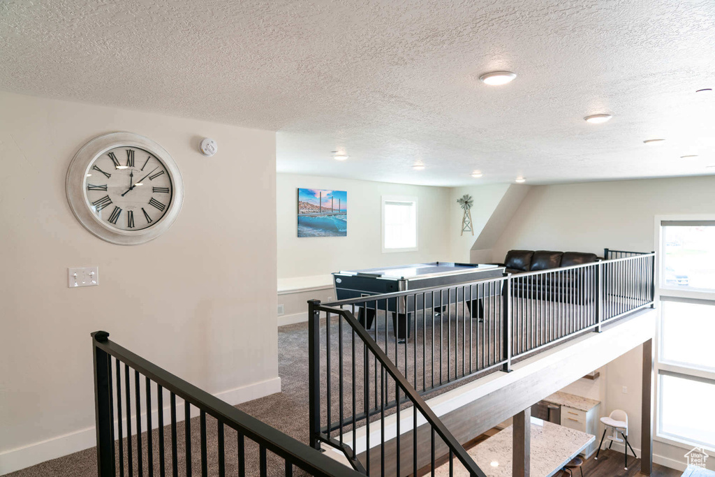 Hall featuring an upstairs landing, baseboards, a textured ceiling, and carpet flooring
