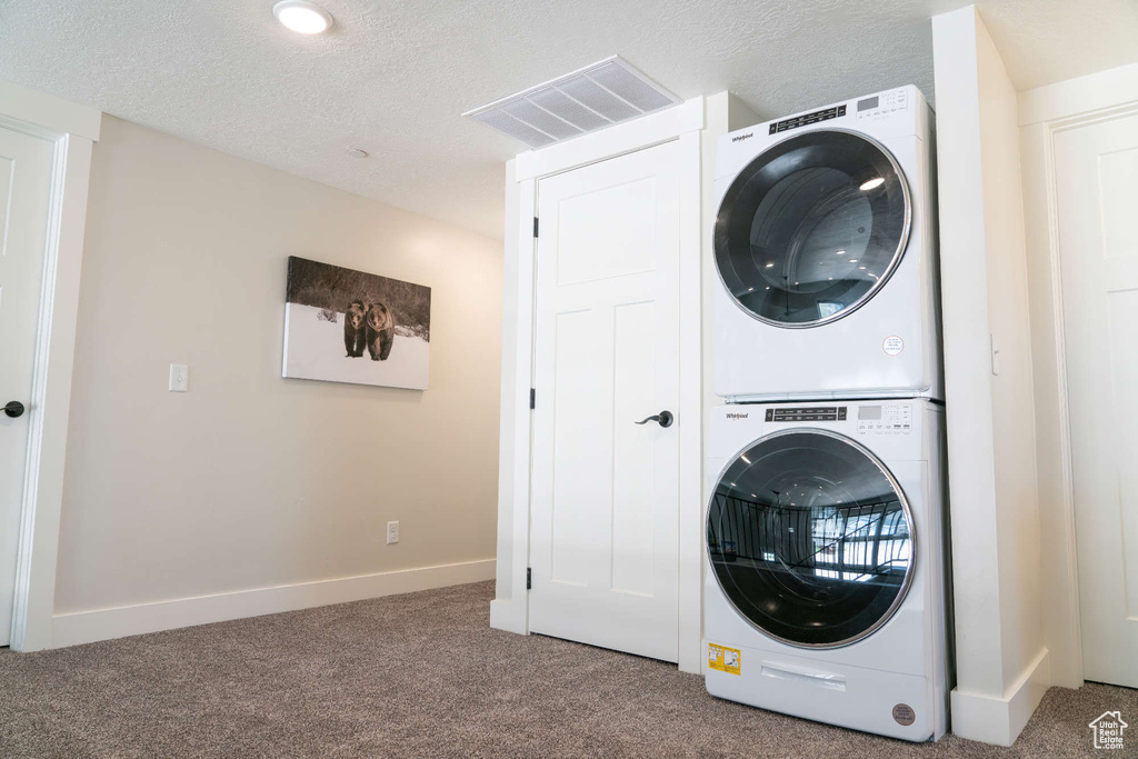 Laundry room with stacked washer and clothes dryer, carpet floors, baseboards, and a textured ceiling