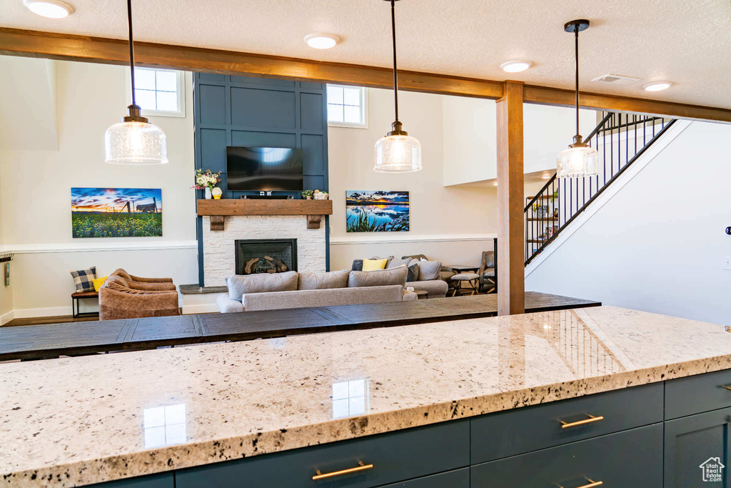 Kitchen featuring light stone countertops, a textured ceiling, decorative light fixtures, a fireplace, and baseboards