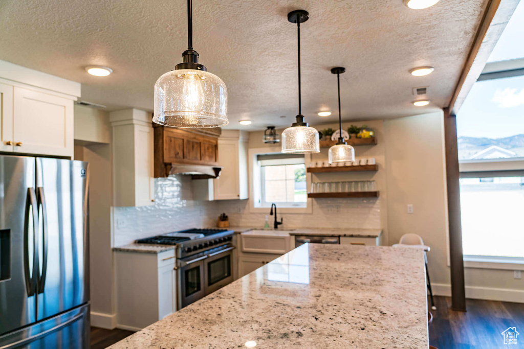 Kitchen featuring appliances with stainless steel finishes, baseboards, tasteful backsplash, a textured ceiling, and light stone countertops