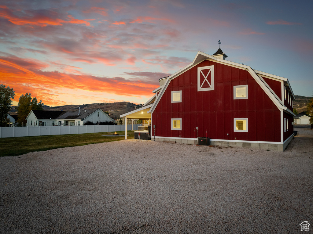 Property exterior at dusk featuring a barn, a gambrel roof, central AC, an outbuilding, and an attached carport