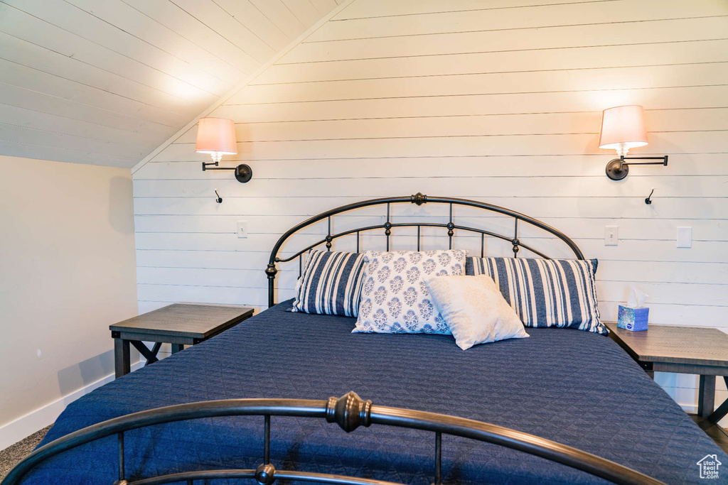 Bedroom featuring vaulted ceiling, wooden walls, baseboards, and carpet floors