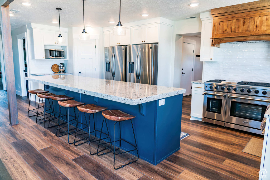 Kitchen featuring stainless steel appliances, tasteful backsplash, white cabinets, dark wood-style flooring, and a textured ceiling