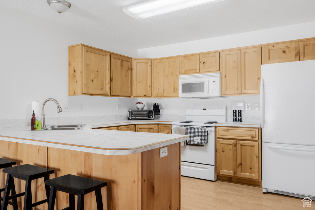Kitchen with white appliances, a sink, light brown cabinets, and a peninsula