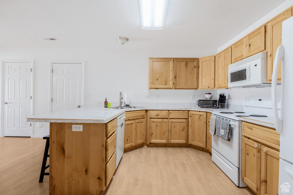 Kitchen with white appliances, a sink, a peninsula, light wood finished floors, and light brown cabinets