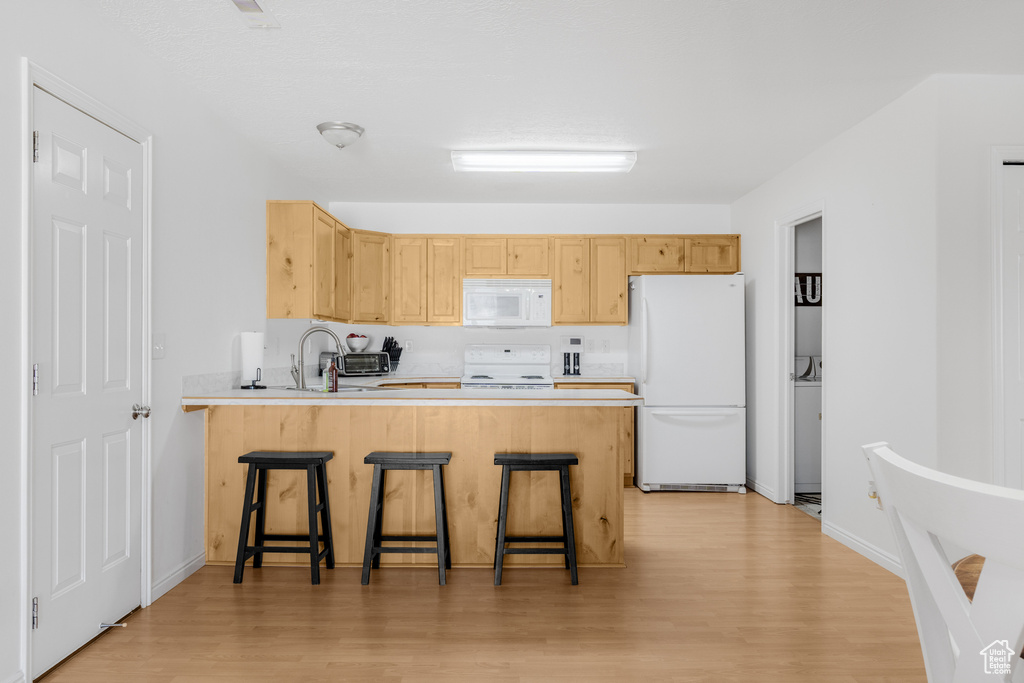 Kitchen featuring white appliances, light brown cabinetry, a peninsula, and light wood-style floors