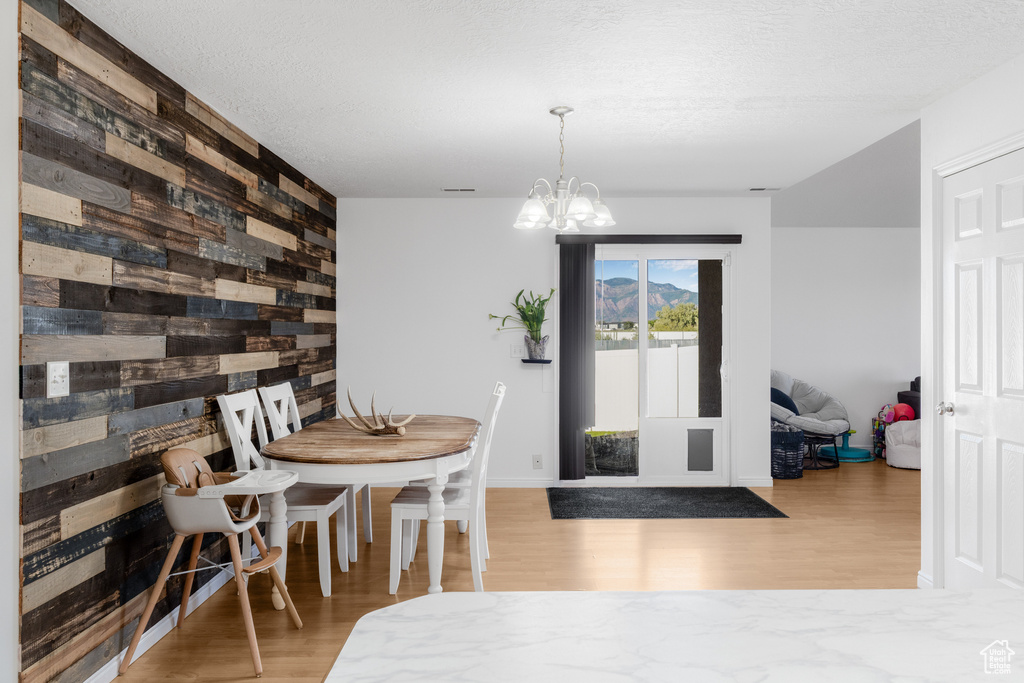 Dining space featuring wood walls, wood finished floors, a chandelier, an accent wall, and baseboards