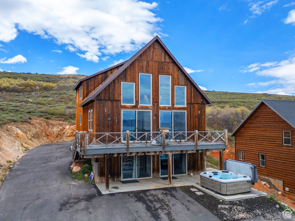 Back of property featuring a hot tub, a wooden deck, and a patio