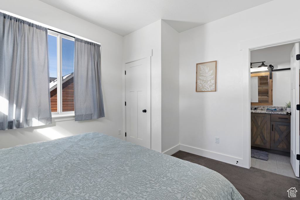 Bedroom featuring dark carpet, baseboards, and connected bathroom