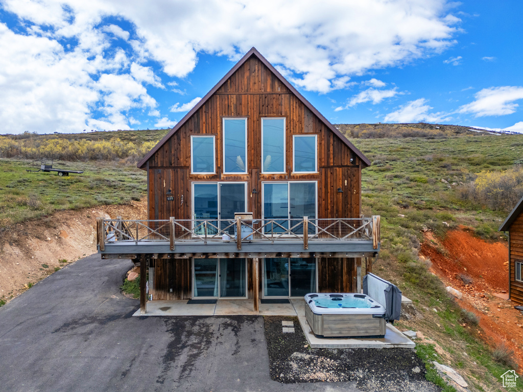 Back of property featuring a deck, a patio area, and a hot tub