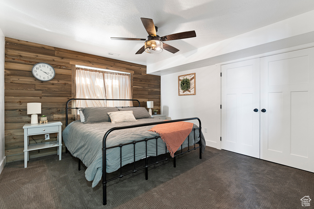 Bedroom featuring wood walls, dark carpet, a closet, a ceiling fan, and baseboards