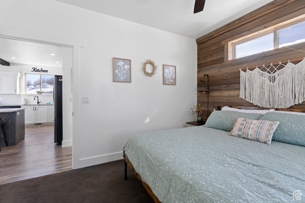 Bedroom featuring wooden walls, a sink, freestanding refrigerator, ceiling fan, and baseboards