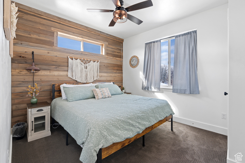 Bedroom featuring wooden walls, carpet, baseboards, an accent wall, and ceiling fan