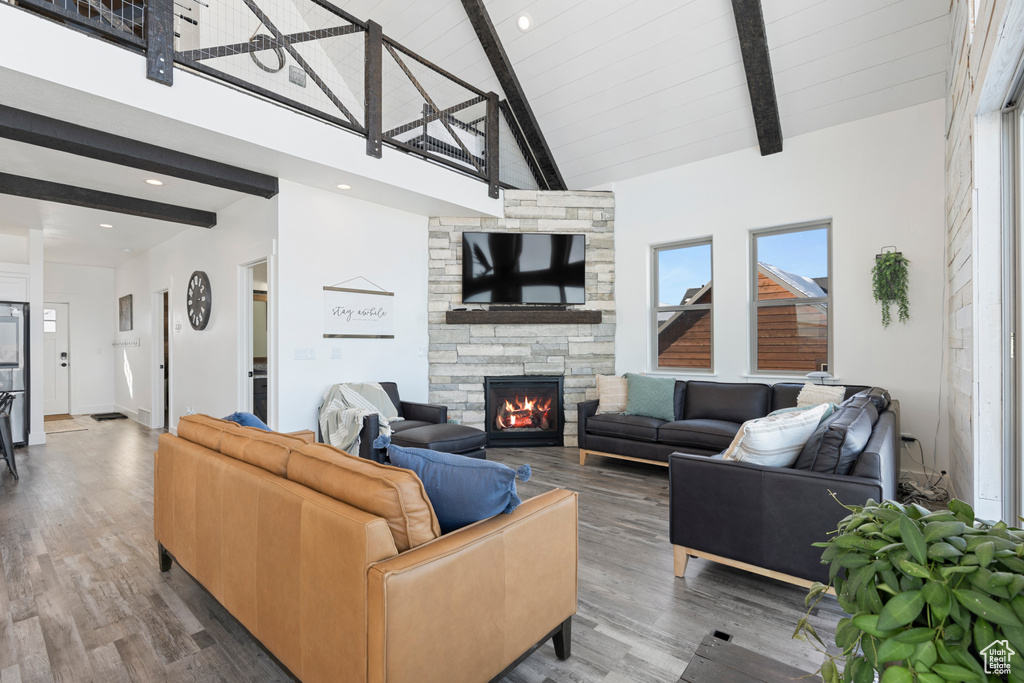 Living room with beamed ceiling, a stone fireplace, wood finished floors, and high vaulted ceiling