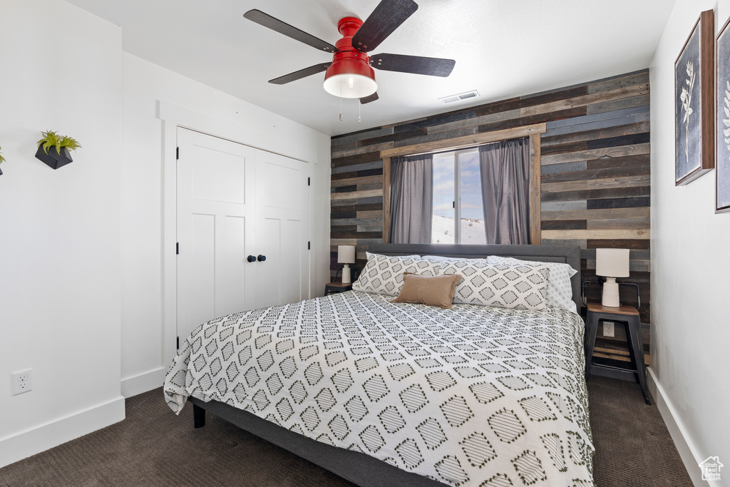 Bedroom with an accent wall, dark colored carpet, baseboards, wooden walls, and ceiling fan