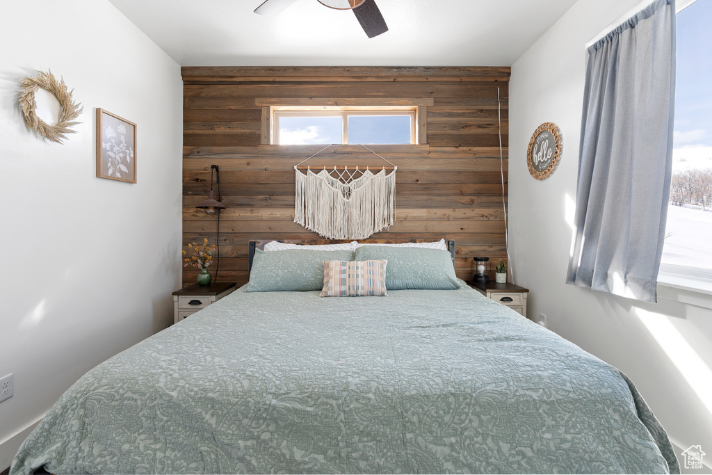 Bedroom featuring wood walls, multiple windows, an accent wall, and ceiling fan