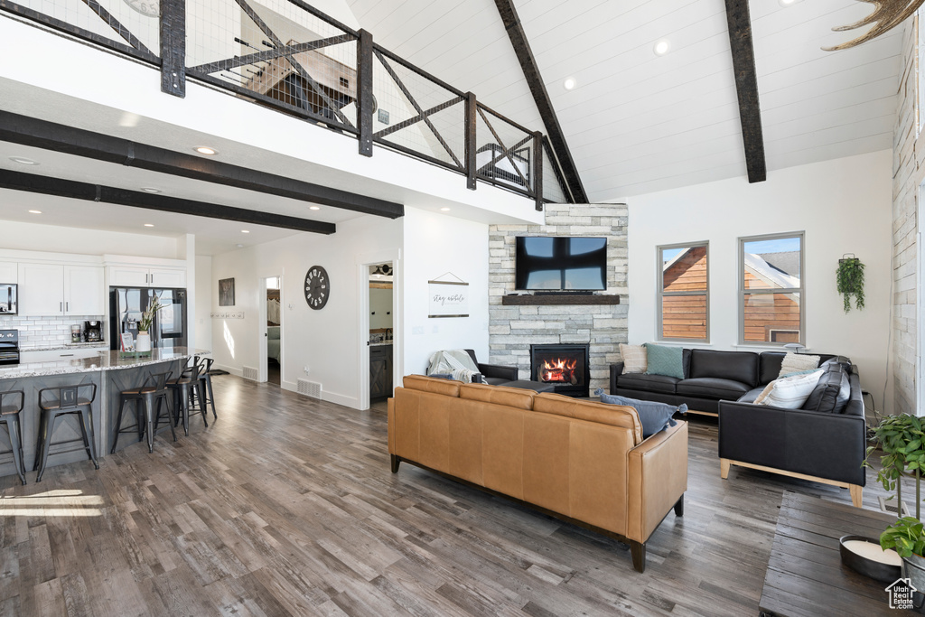 Living room with high vaulted ceiling, a stone fireplace, beamed ceiling, dark wood-style floors, and recessed lighting