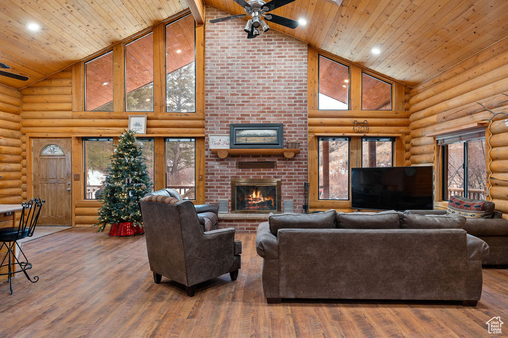 Living room featuring high vaulted ceiling, a ceiling fan, log walls, a fireplace, and wood ceiling