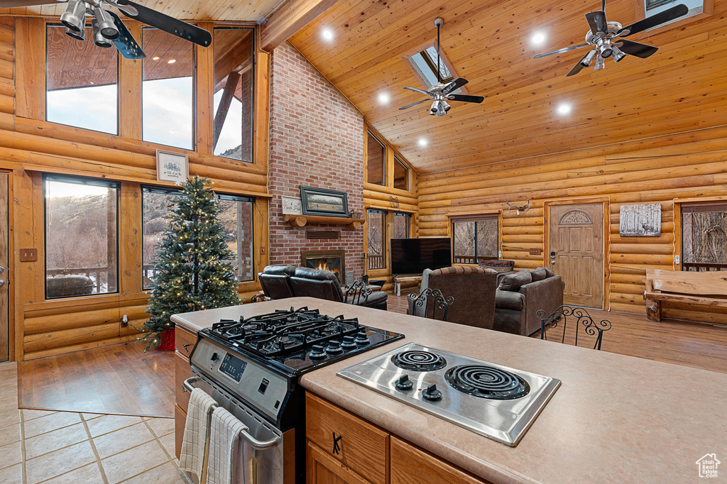 Kitchen with a ceiling fan, stainless steel appliances, high vaulted ceiling, rustic walls, and a brick fireplace