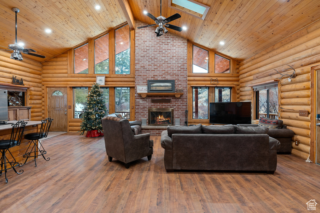 Living room with ceiling fan, high vaulted ceiling, a fireplace, log walls, and wood finished floors