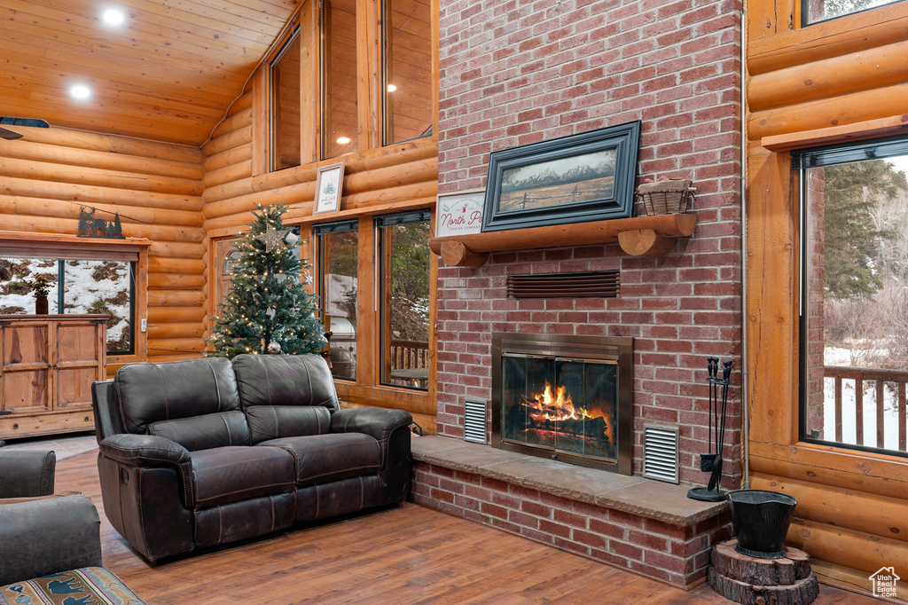 Living area featuring a fireplace, high vaulted ceiling, log walls, wood finished floors, and wooden ceiling
